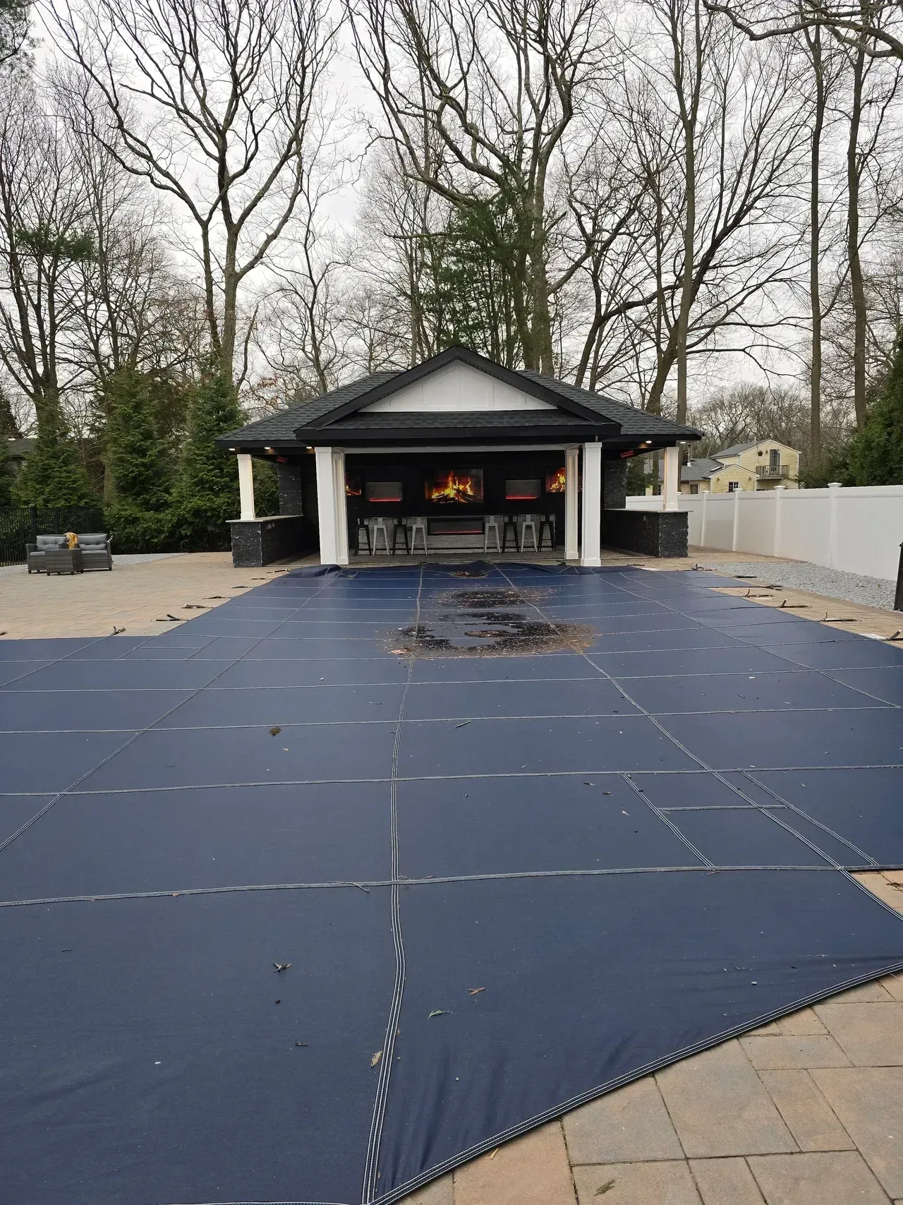 A large blue tarp is covering a swimming pool in front of a house.