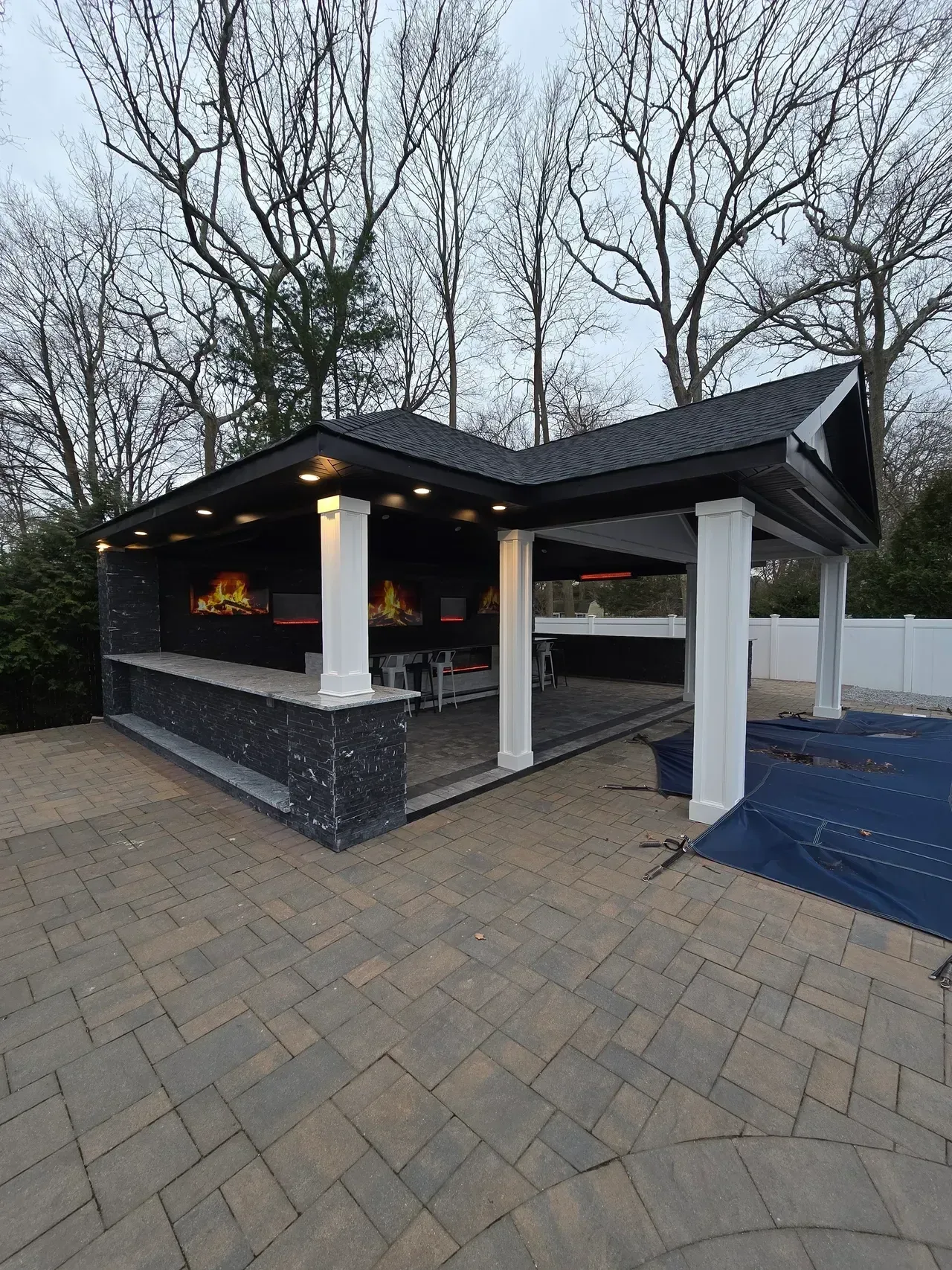 A gazebo with a fireplace and a brick patio in front of a pool.