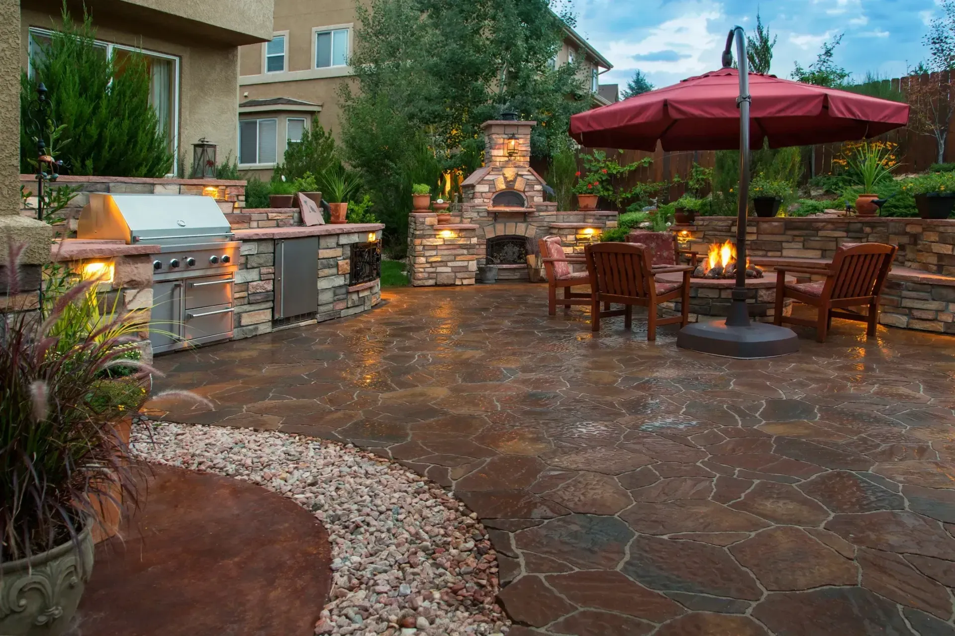 Outdoor patio with grill, fireplace, seating, and umbrella. Stone features and brown paving.