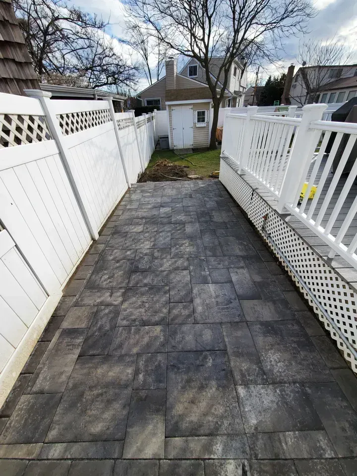 A walkway leading to a house with a white fence.