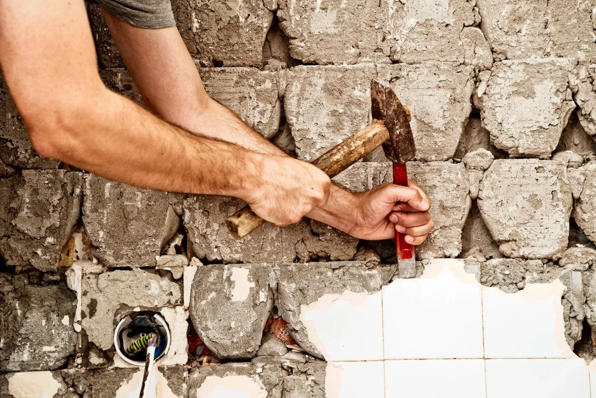 A man is hammering a brick wall with a hammer.