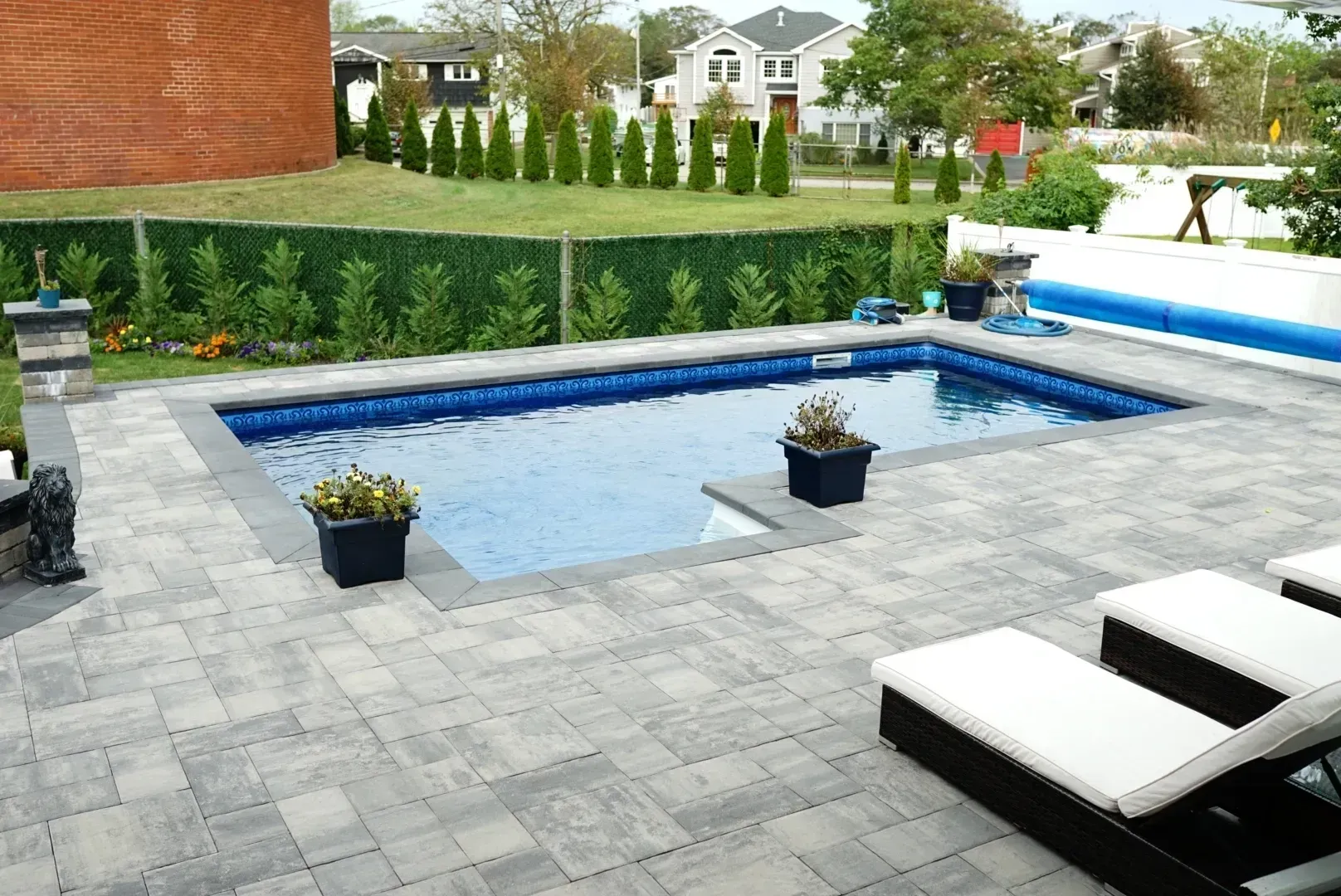 A large swimming pool is surrounded by a brick patio and chairs.