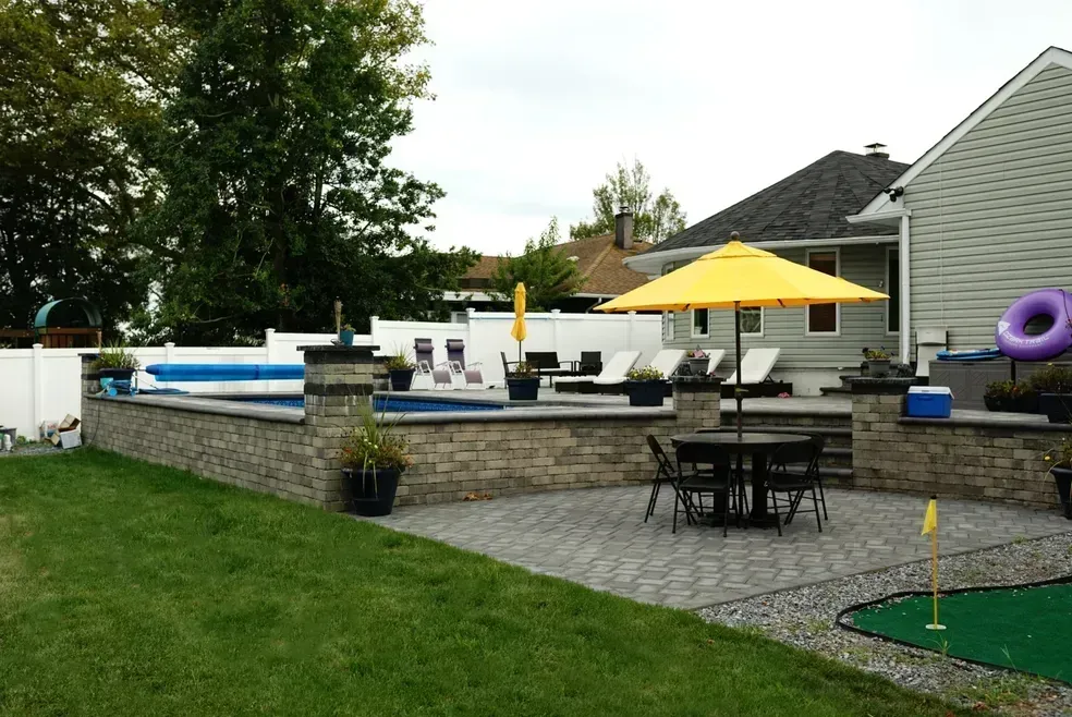 A backyard with a pool table and chairs and a yellow umbrella