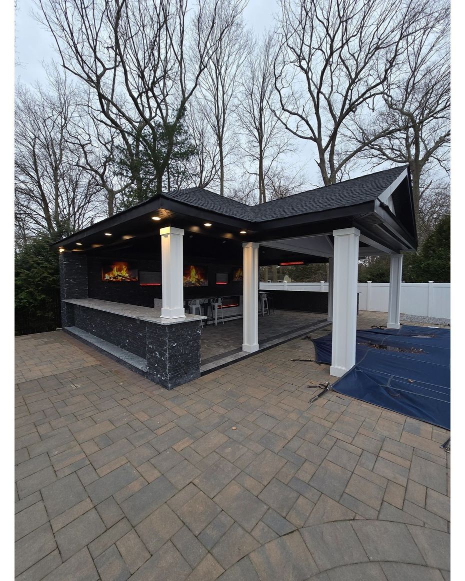 A gazebo with a fire place and a brick patio in front of it.