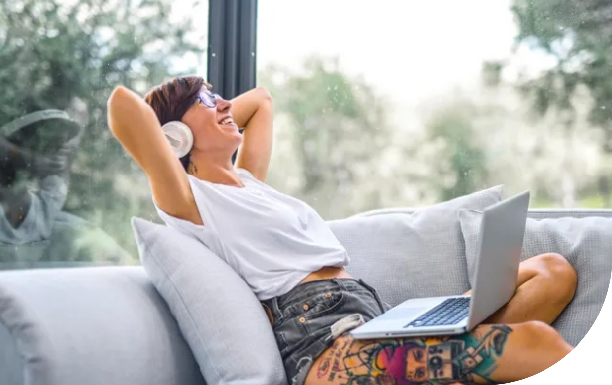 A woman is sitting on a couch with a laptop and headphones on.