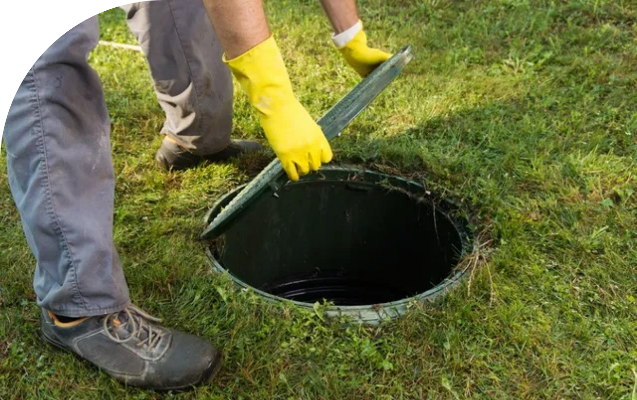 A person wearing yellow gloves is opening a septic tank.