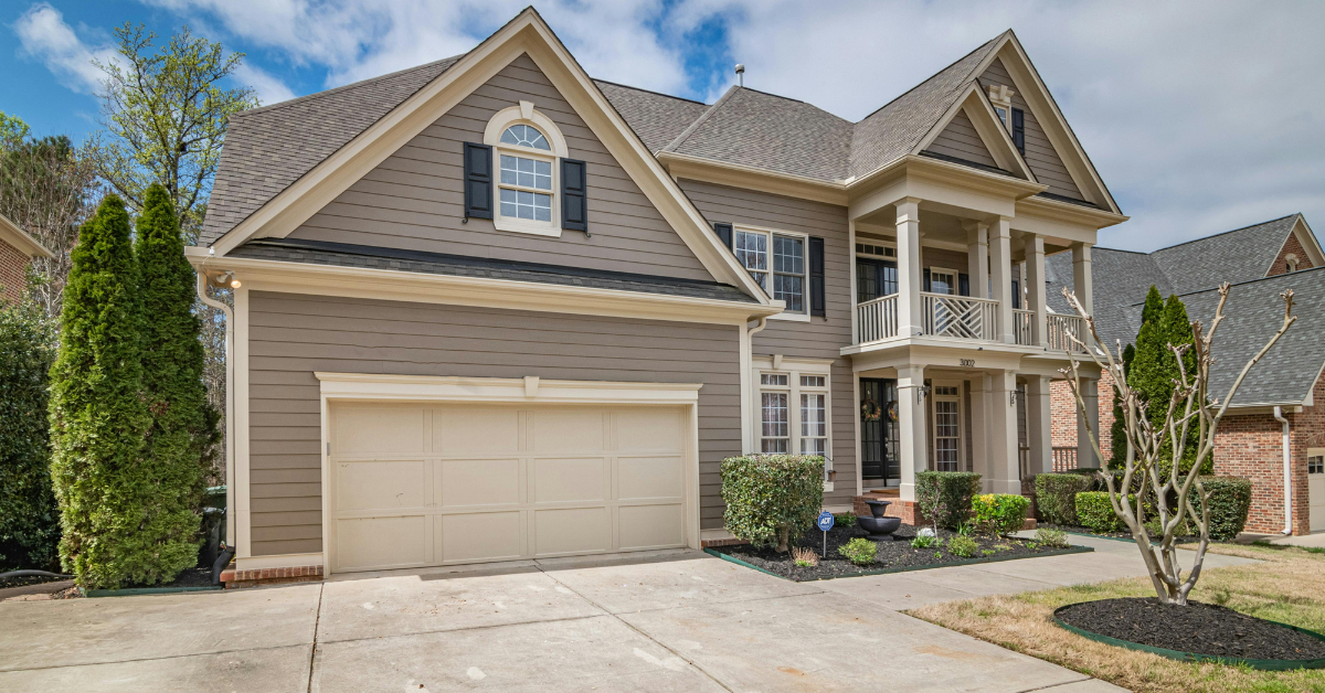 Two-story beige house with a covered porch and attached garage on a concrete driveway.