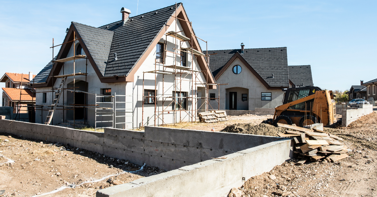 An infill house under a clear blue sky, with scaffolding, construction debris, and a yellow tractor.