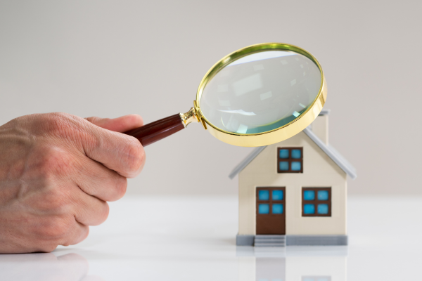 A person is holding a magnifying glass over a model house.