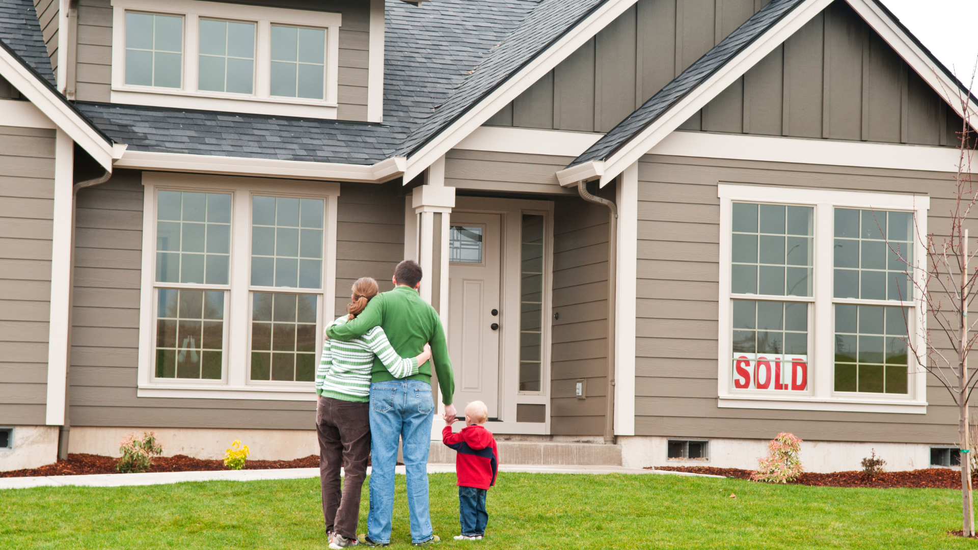 A family standing in front of a house that has a sold sign on it