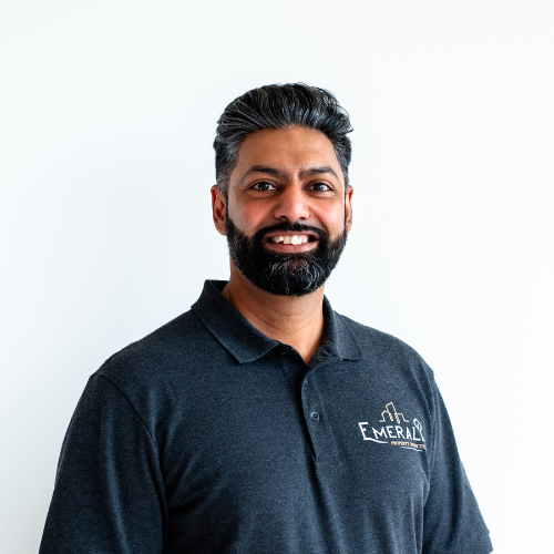 Sukh Rasode is smiling, wearing a dark gray polo shirt. White background.