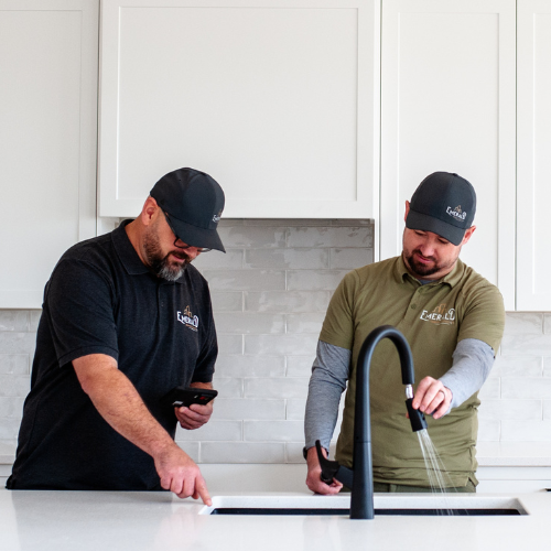 Dennis and Ryan examine a black faucet in a white kitchen sink.