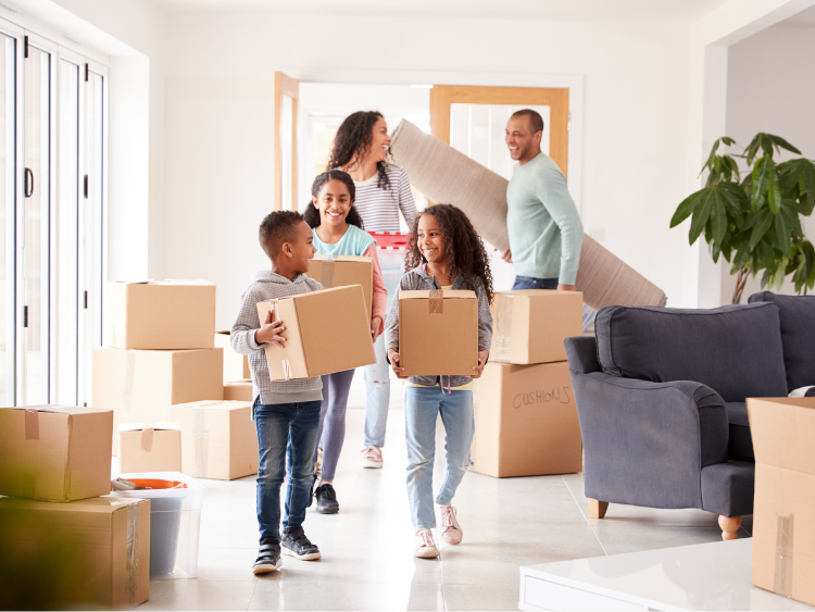 A family is carrying cardboard boxes into a new home.