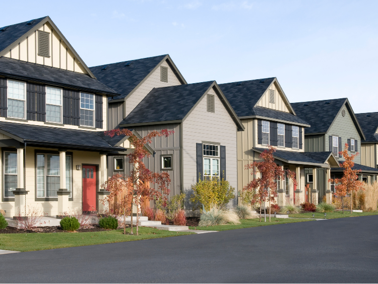Row of two-story houses with gabled roofs and varied neutral paint colors, set against a blue sky.