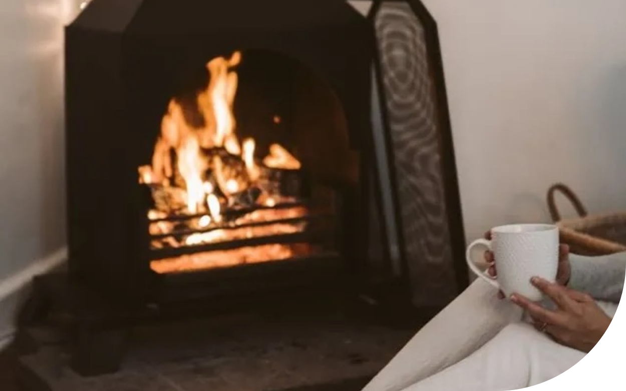 A person is sitting in front of a fireplace holding a cup of coffee.