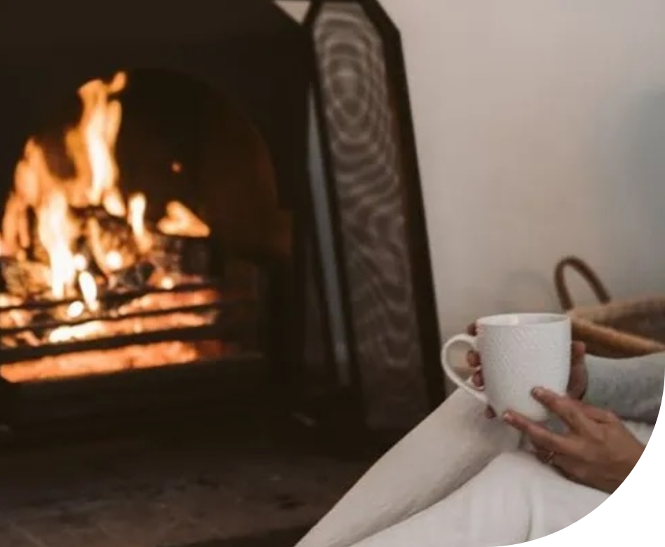 A woman is enjoying a fireplace while holding a cup of coffee.