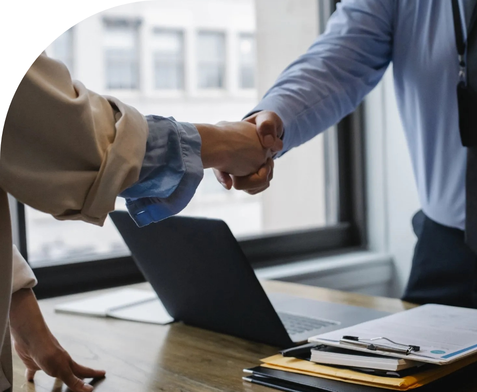 A man and woman are shaking hands in front of a laptop.