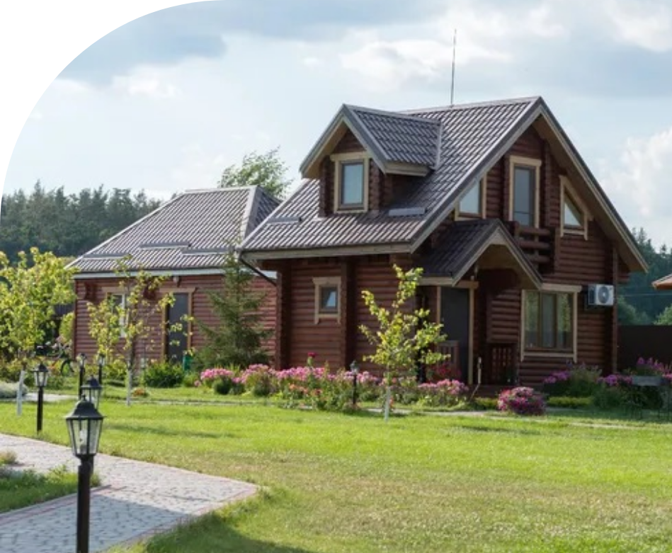 A large wooden house with a gray roof is in the middle of a lush green field.