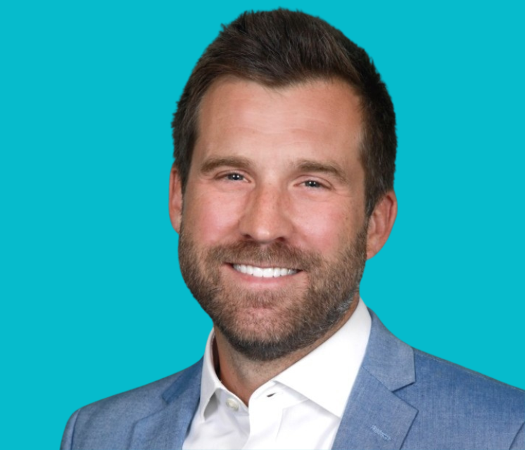 A man with a beard is wearing a blue suit and white shirt and smiling.