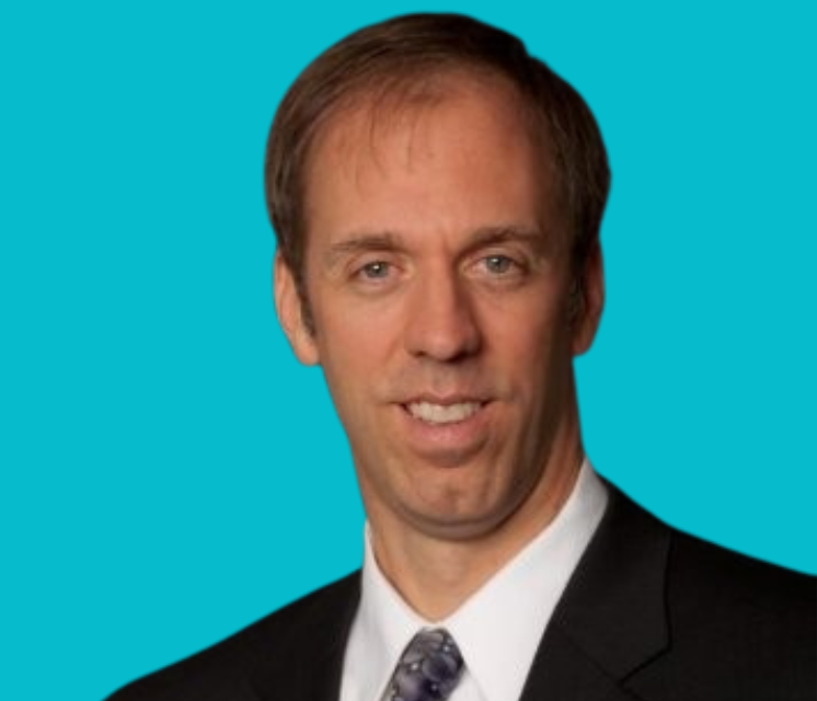 A man in a blue shirt is smiling in front of a blue background.