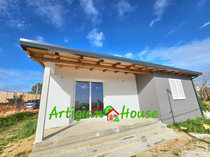 Piccola casa moderna con tetto grigio e pareti bianche e grigie sotto un cielo azzurro.