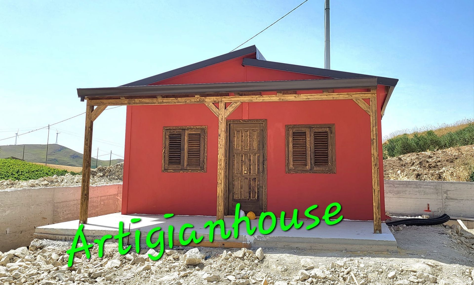 Casa artigianale rossa con veranda e porta in legno sotto un cielo azzurro e terso.
