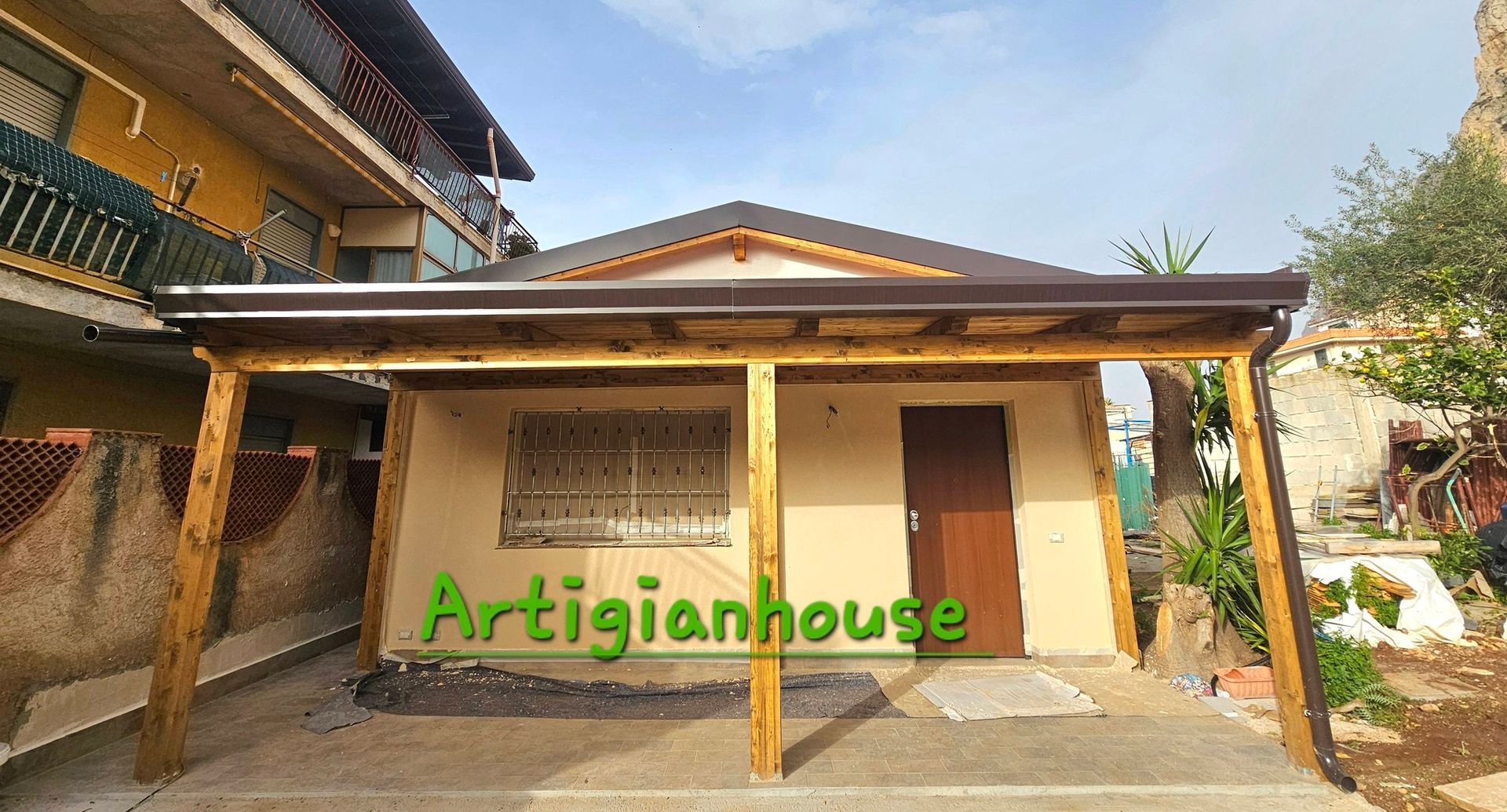 Posto auto coperto in legno di fronte a un edificio color marrone chiaro con porta marrone.