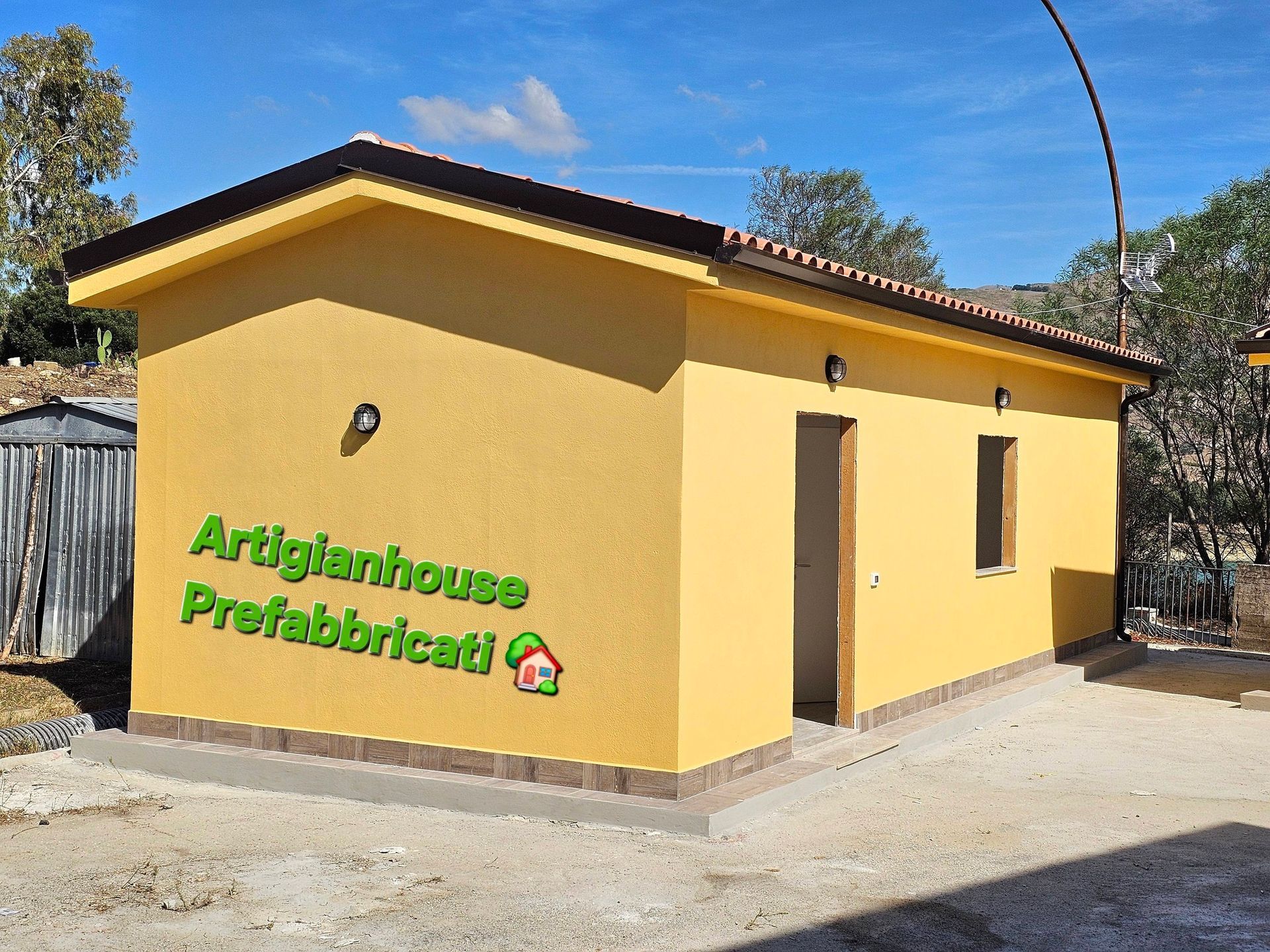 Edificio prefabbricato giallo con tetto, porta e finestra marroni. Logo 