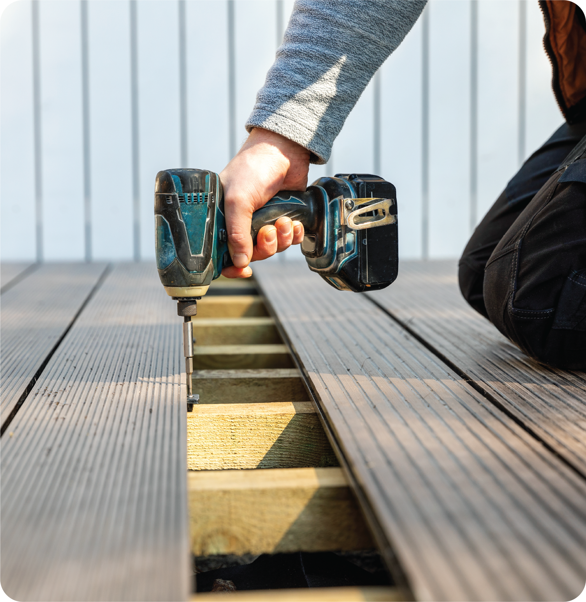 A person is using a drill on a wooden deck.