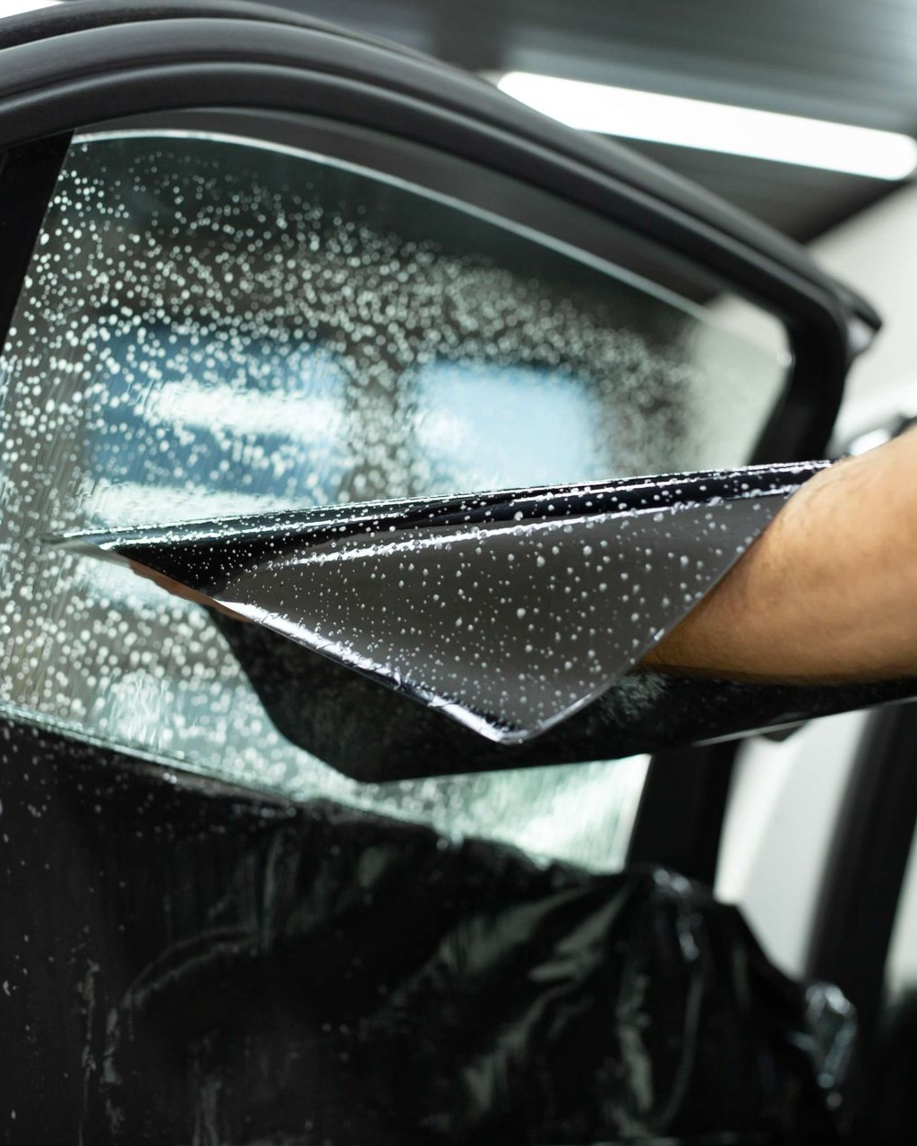 A man is cleaning the wheel of a black car with a sponge.