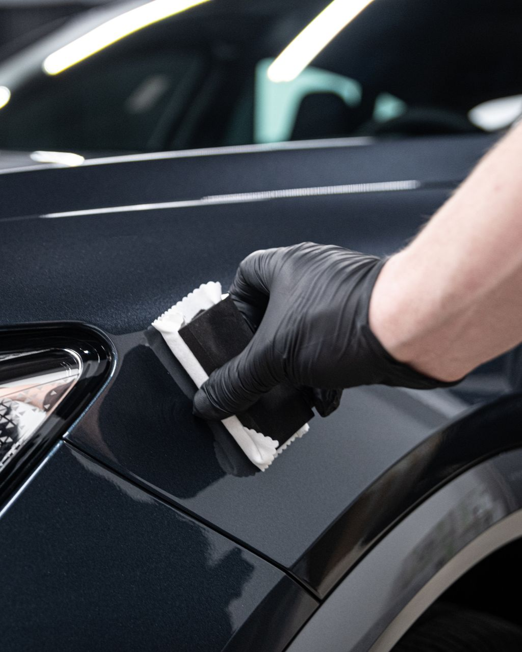 Person in black glove applying ceramic coating to a dark blue car's fender.