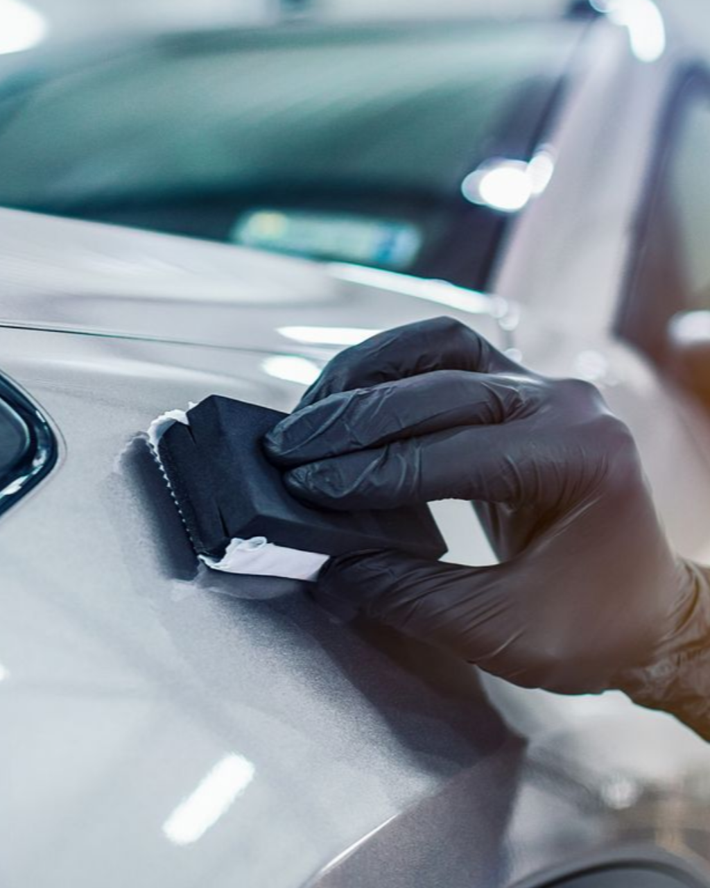 Person in black gloves applying ceramic coating to car paint.