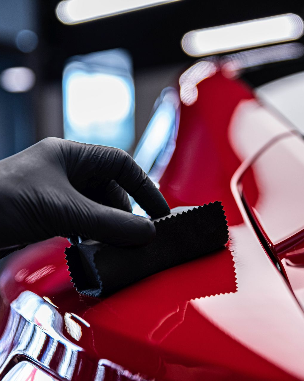 A man is cleaning the wheel of a black car with a sponge.
