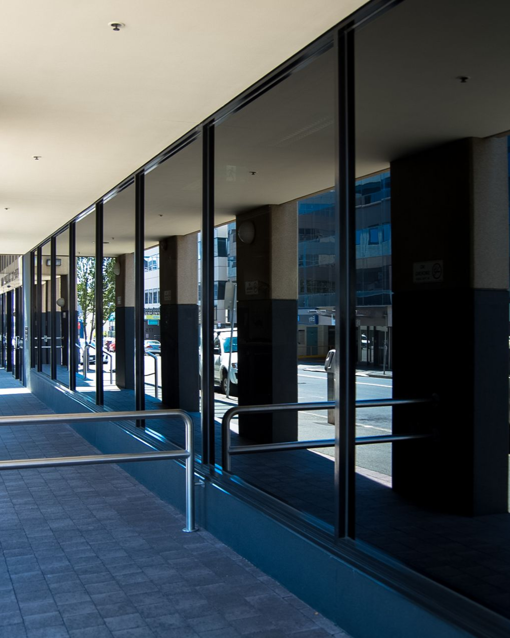 Building exterior with long row of glass windows, dark pillars, and reflective glass.
