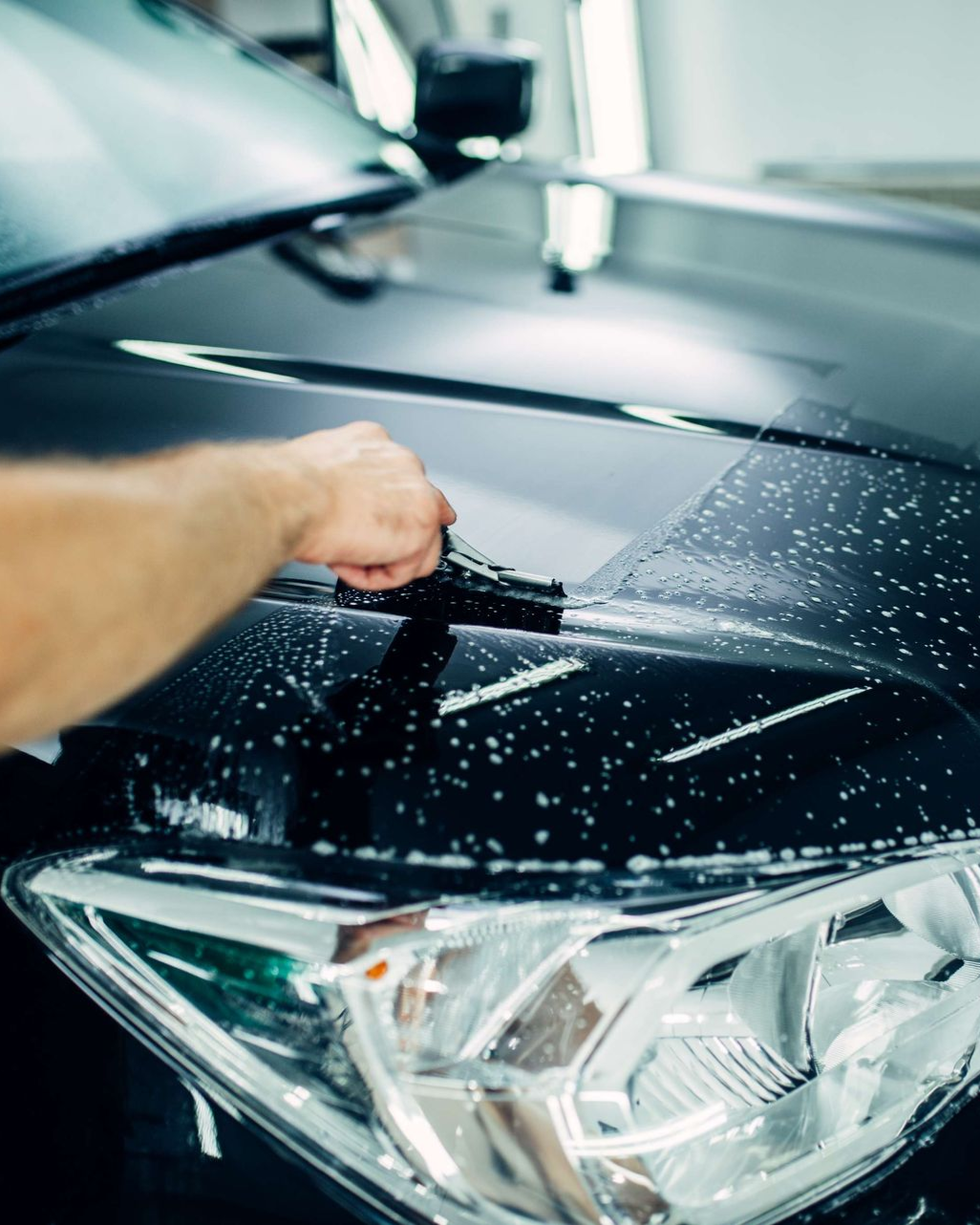 Hand applying protective film to a black car's hood.