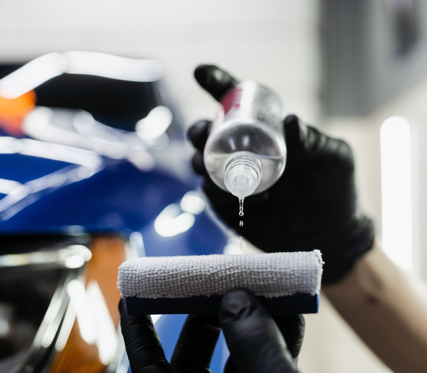 A person is polishing the hood of a blue car.