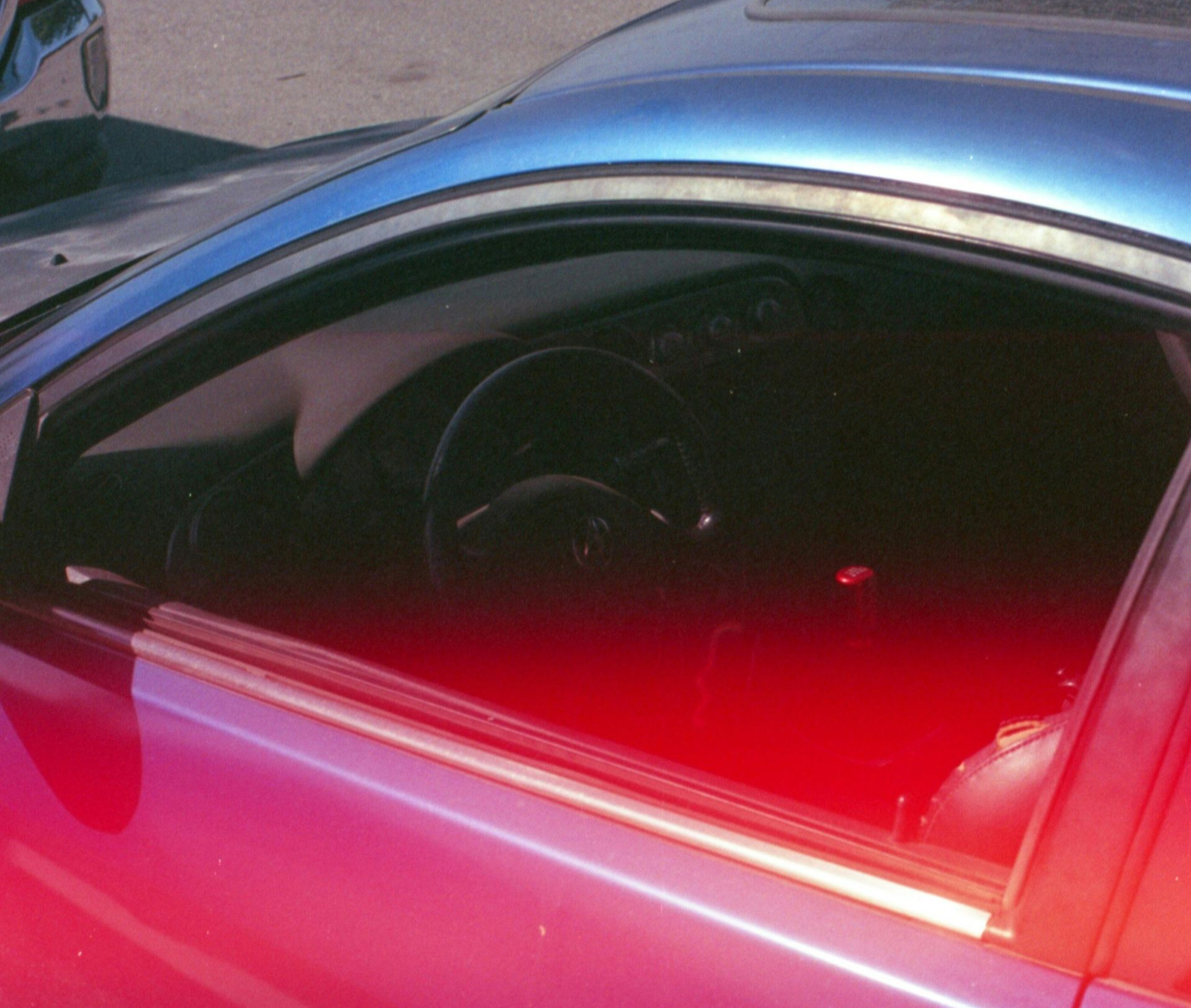 A person in black gloves uses a green tool to apply something to a car's dark side.