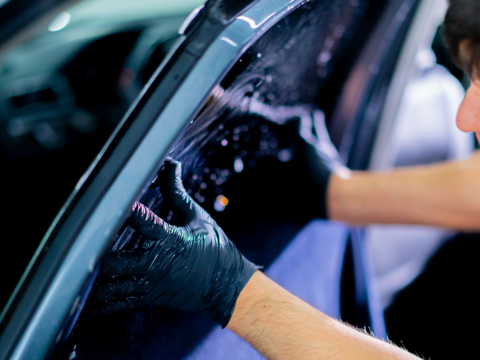 Person in black gloves applying window tint to a car door.