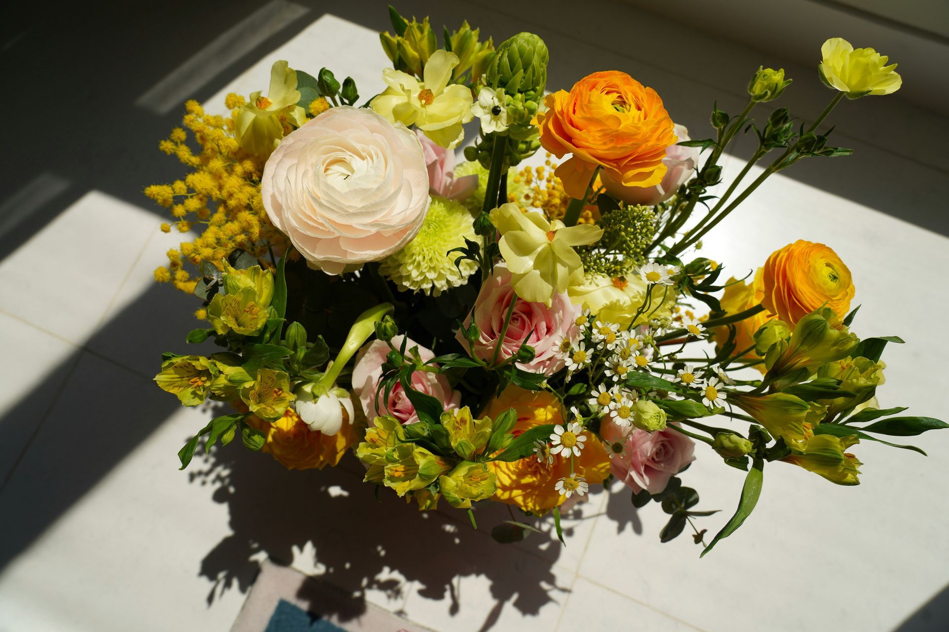 Mixed bouquet of white, yellow, and orange flowers on a sunlit table