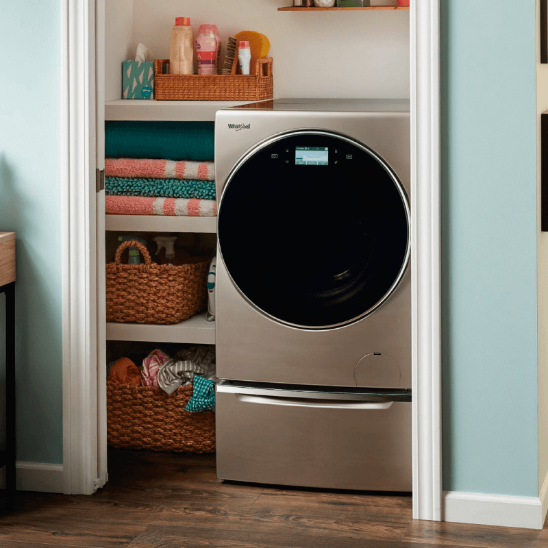 Una lavadora y una secadora están en un armario lleno de ropa.