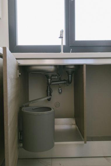 Under-sink kitchen cabinet with plumbing, a metallic basin floor, and a door-mounted grey waste bin.