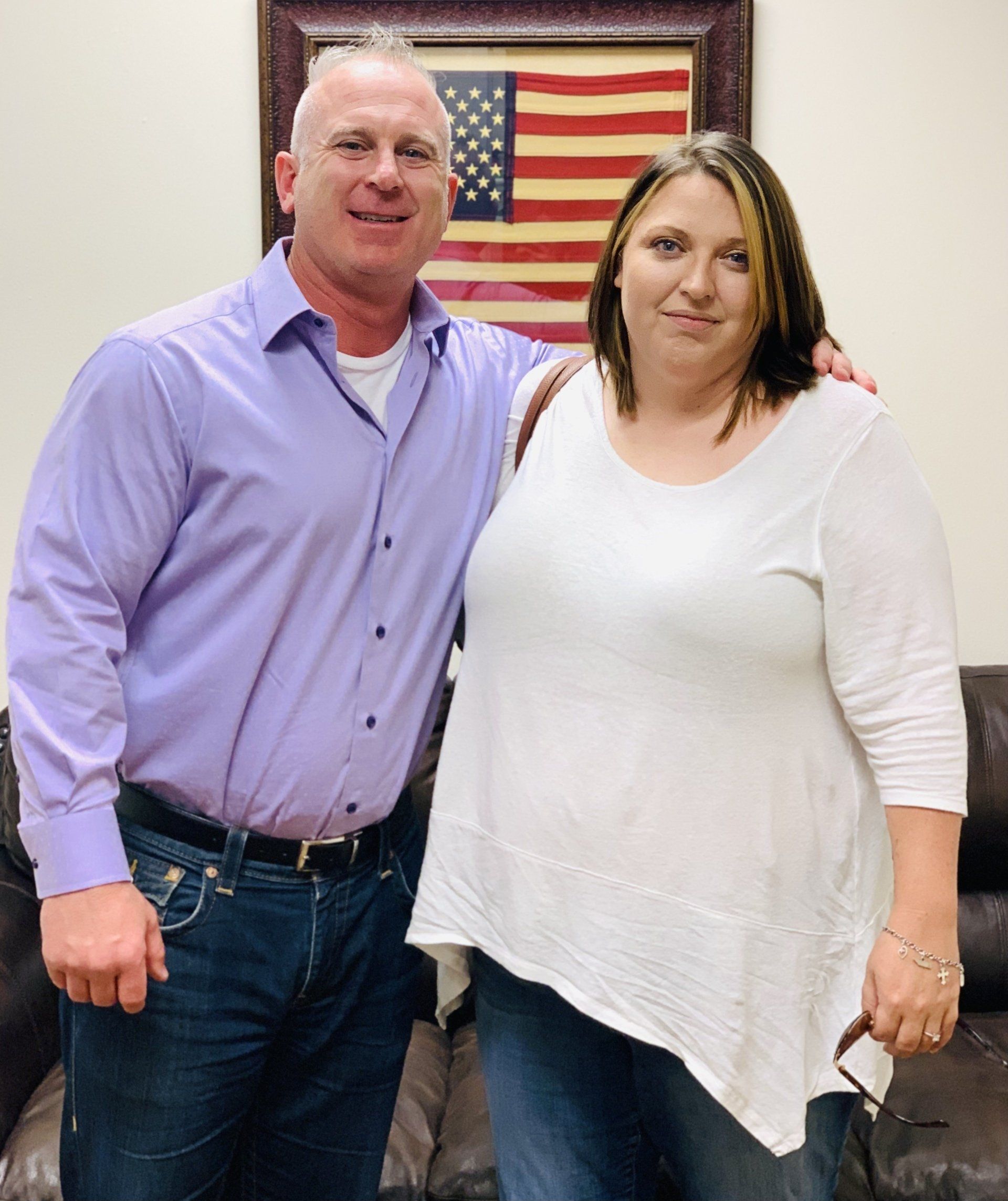 A man and a woman are posing for a picture in front of an american flag.