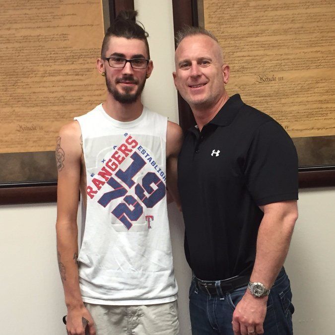 A man wearing a rangers shirt stands next to another man