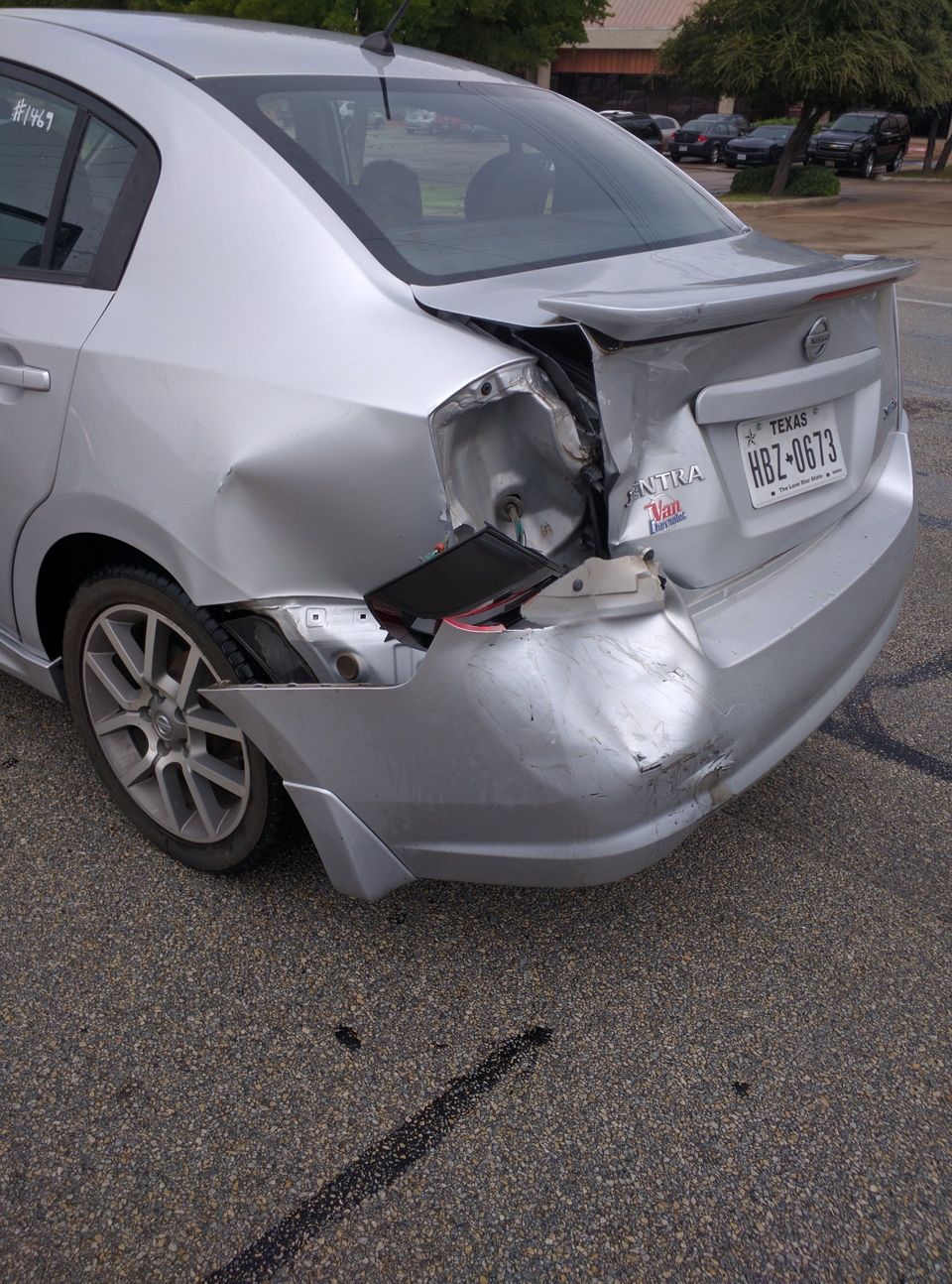 A silver car with a damaged rear end is parked on the side of the road.