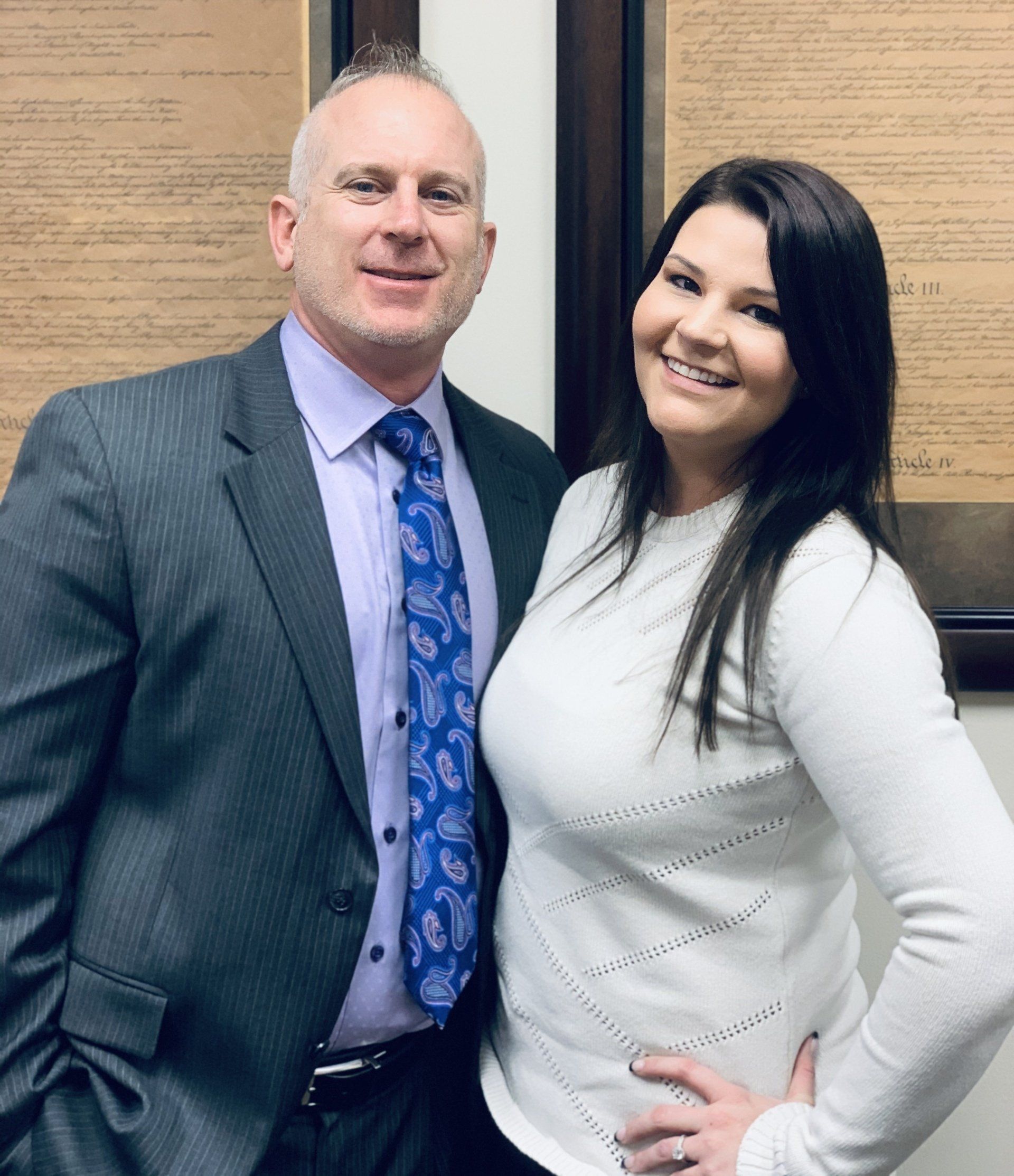 A man in a suit and tie stands next to a woman in a white sweater