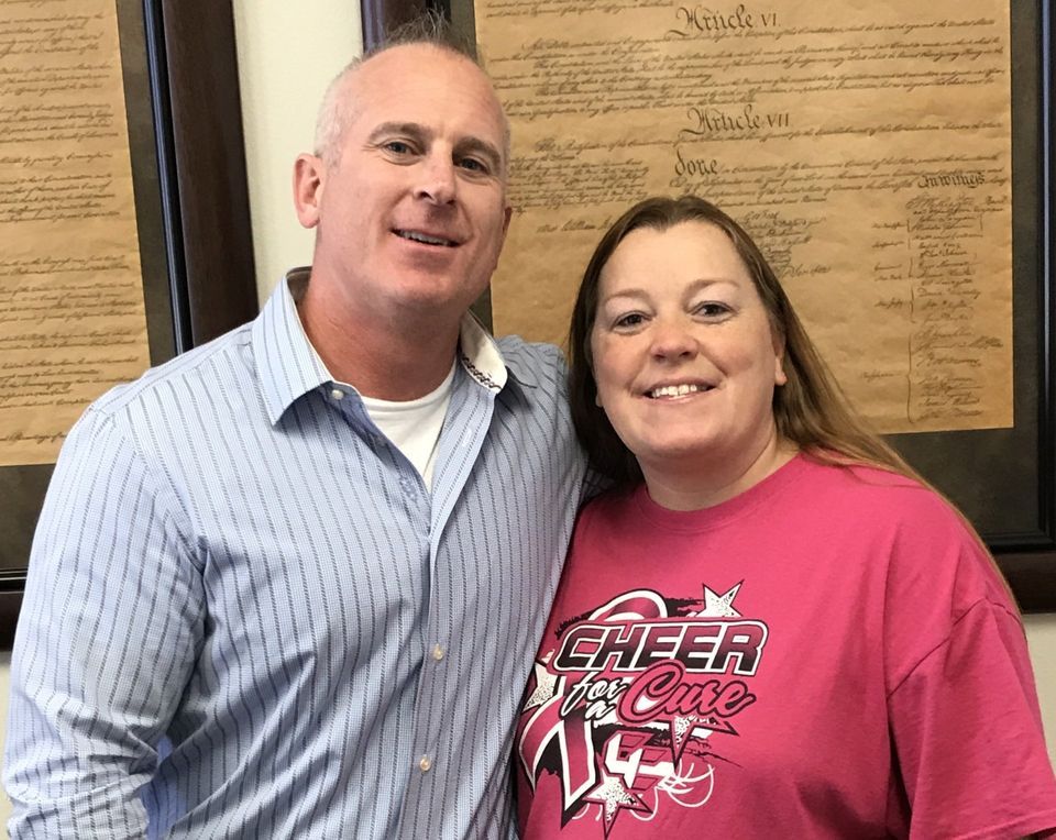 A man and a woman are posing for a picture and the woman is wearing a cheer shirt