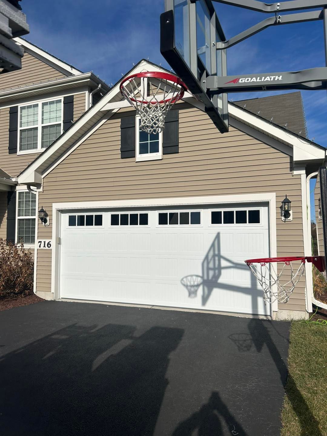 Garage with basketball hoop attached, asphalt driveway, beige siding, and clear sky.