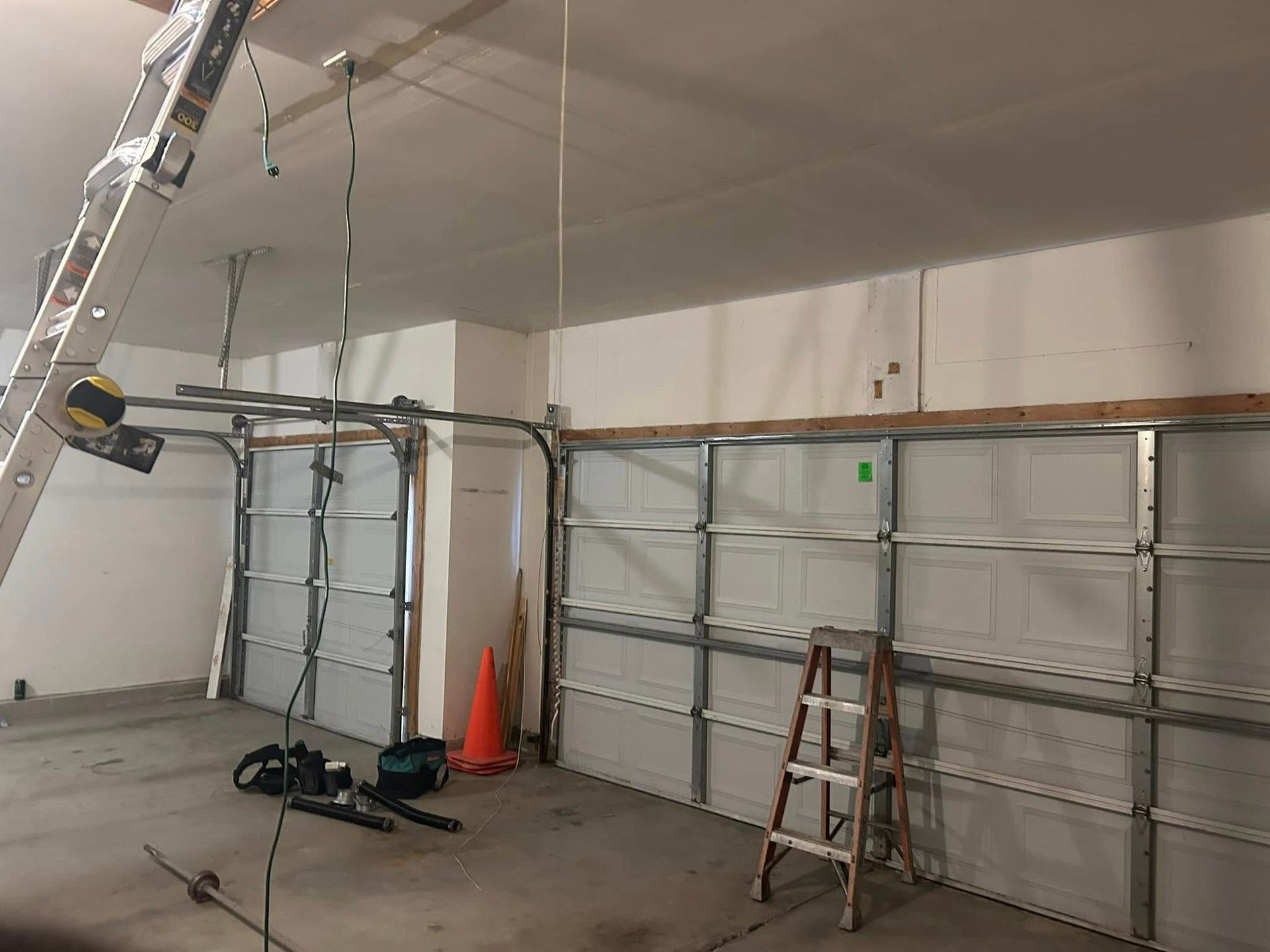 Garage interior with two garage doors, one partially open. Tools and ladders present.