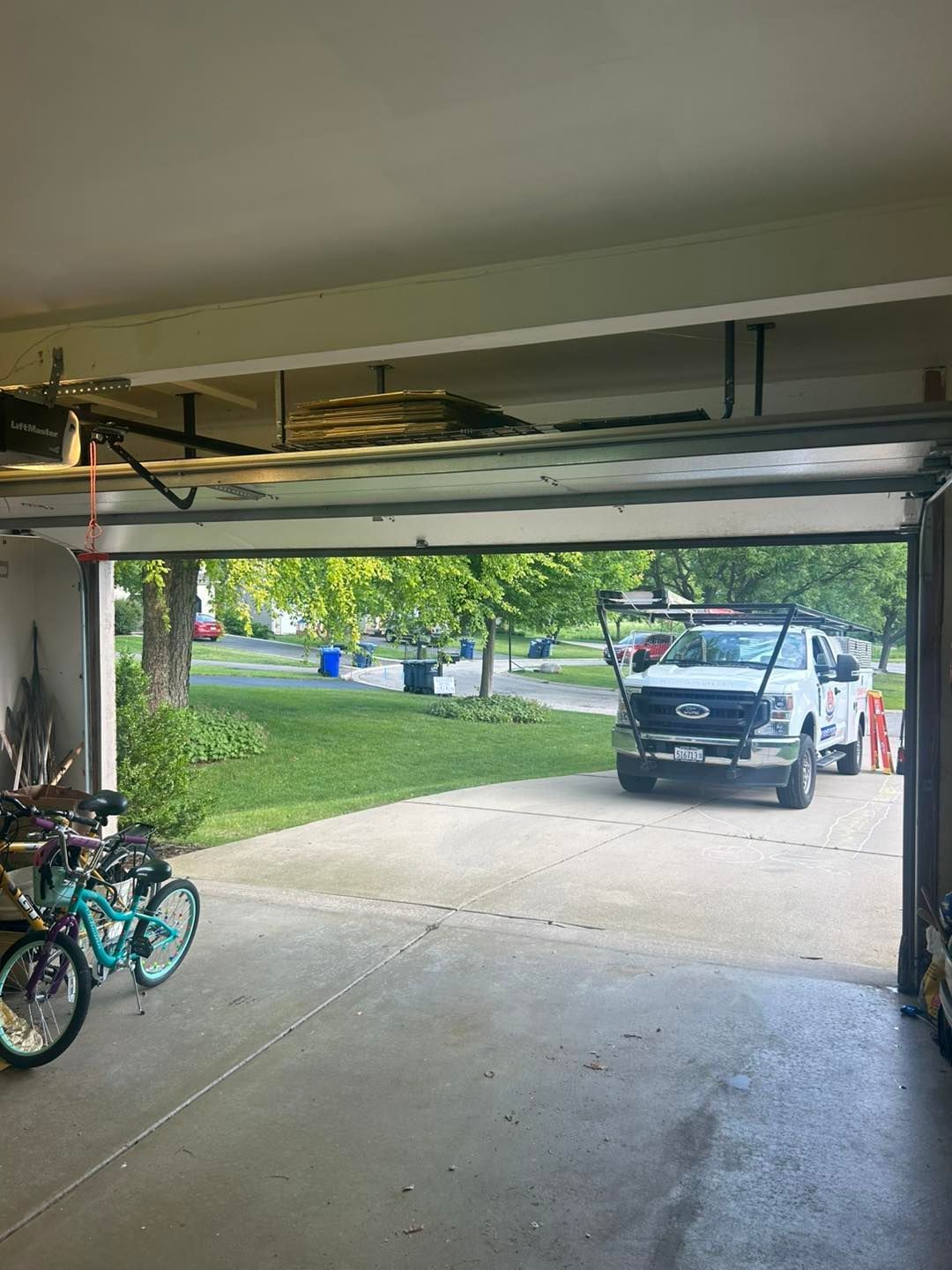 Garage door, bicycles inside. A white service truck is parked outside on the driveway, and a grassy yard is visible.