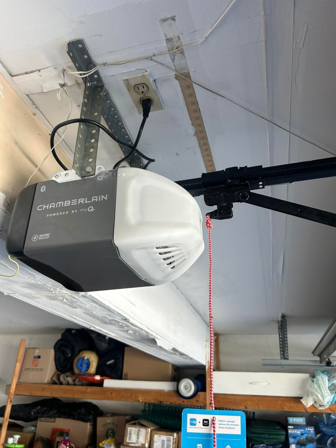 Garage door opener attached to ceiling, with electrical outlet nearby.